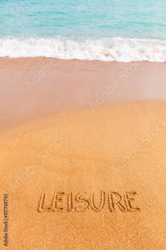 Inscription "LEISURE" made on the beach by the blue sea