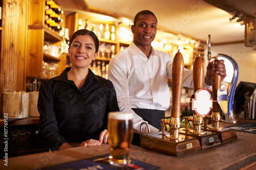 A young man and woman working behind a bar look to camera
