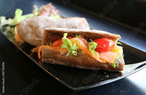 Sandwich with smoked salmon on black plate.