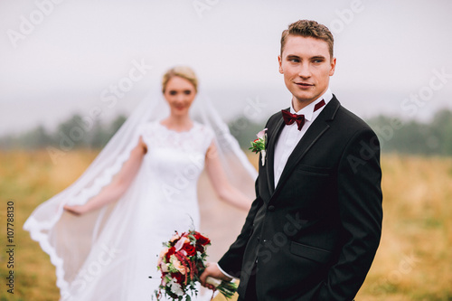 Newlywed bride and groom holding hands in autumn forest field