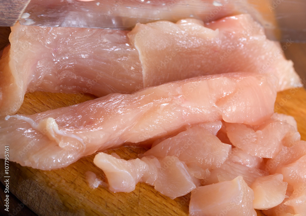 The crude chicken meat cut on pieces on a wooden board The crude chicken meat cut on pieces on a wooden board