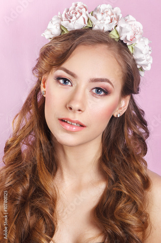 Beautiful young girl with a floral ornament in her hair on a pink background © Elena Kratovich