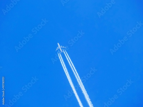 Airplane with chemtrails on blue sky 