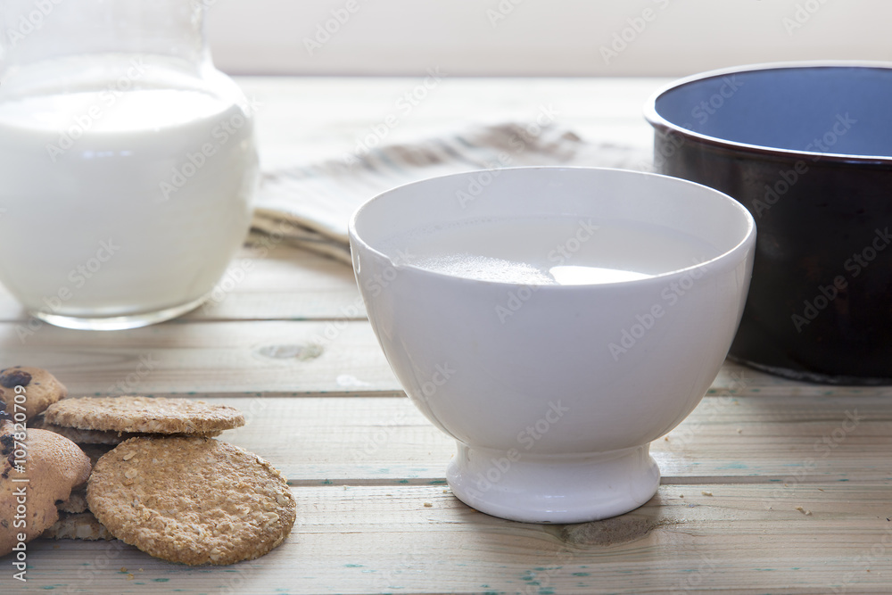 Bowl of milk with biscuits and a saucepan to heat. Healthy breakfast of milk heated in fire without use microwave, cookies and jar of milk Bowl of milk with biscuits and a saucepan to heat. Healthy breakfast of milk heated in fire without use microwave, cookies and jar of milk