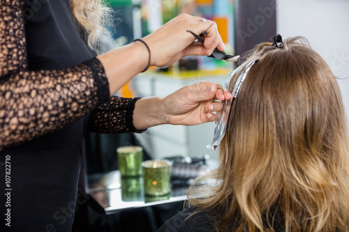 Hairdresser Highlighting Client's Hair In Salon