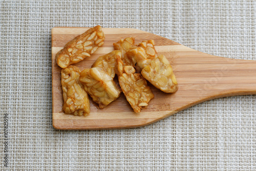 Fried Tempeh in wooden spatula on textured background. Tempeh is made from soy bean and popular in some part of Asia.

