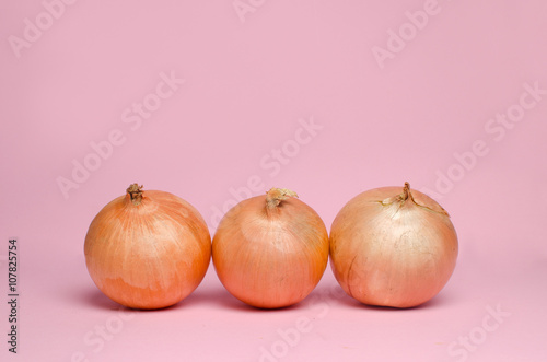 Whole three onions on a pink background