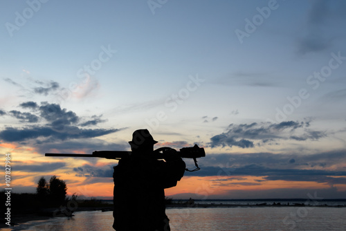 Silhouette of the hunter with the shot gun on a sunset background © river34