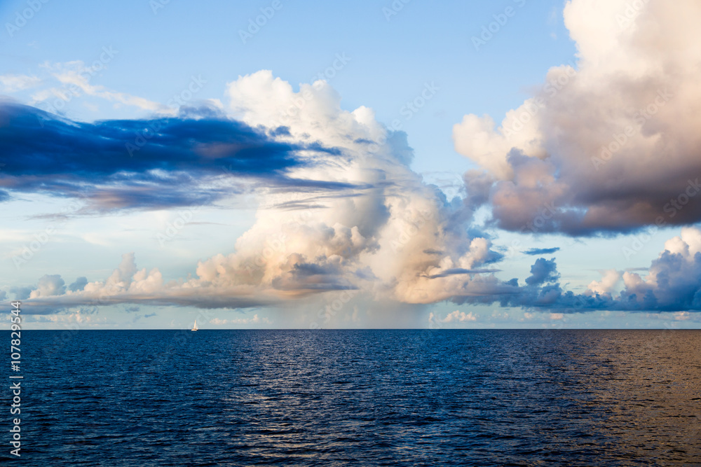 Blue ocean, light of large clouds reflected on surface, rainbow