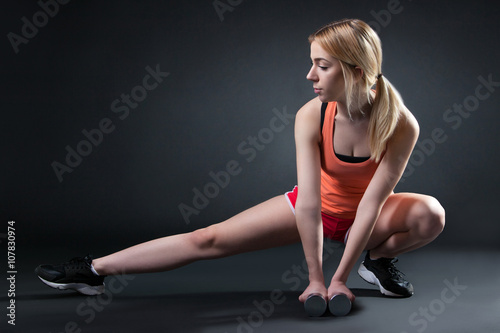 young sporty female in sportswear exercising with dumbbell on a black background photo