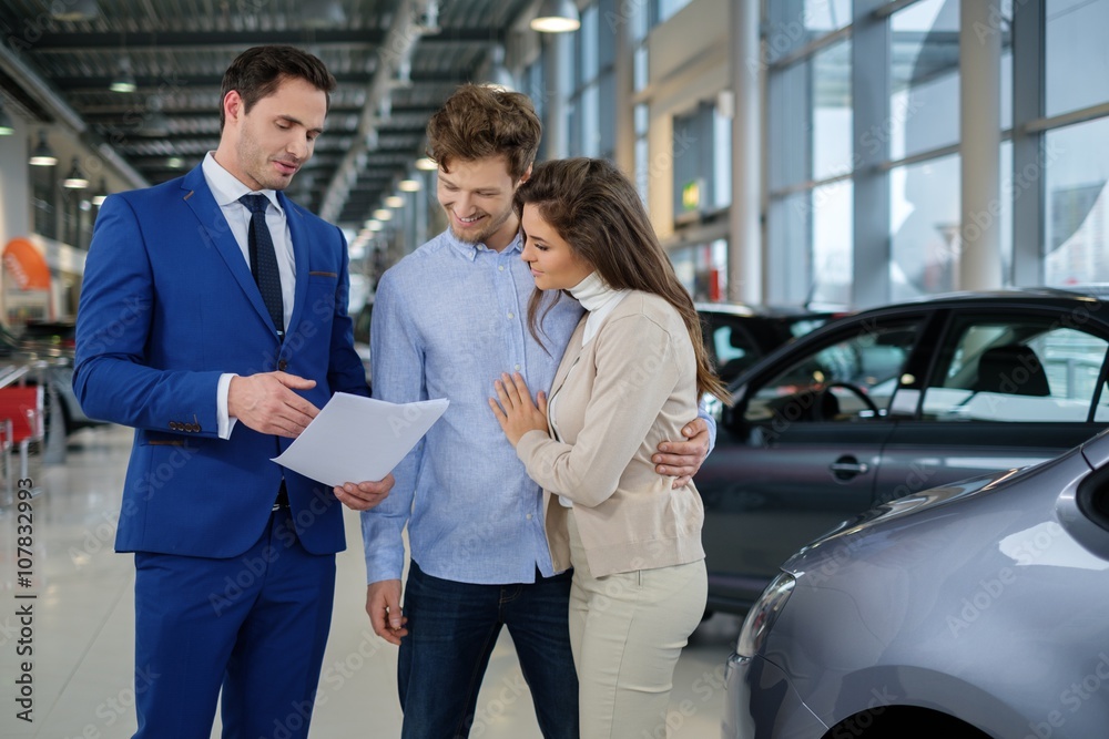 Salesman talking to a young couple at the dealership showroom. Salesman talking to a young couple at the dealership showroom.