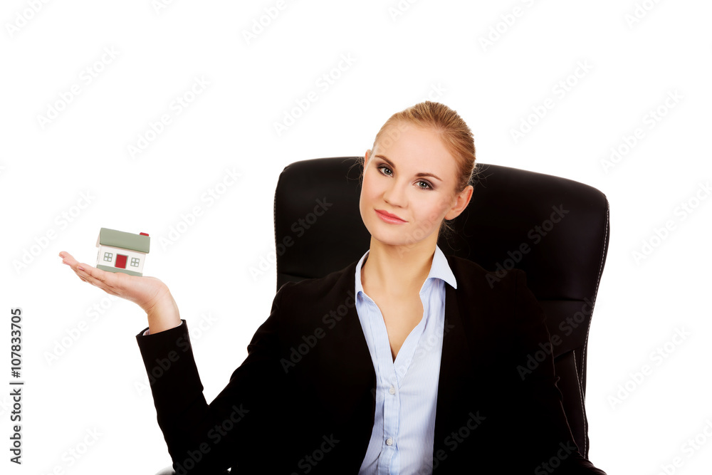 Smiling business woman sitting on a chair and holding house model Smiling business woman sitting on a chair and holding house model