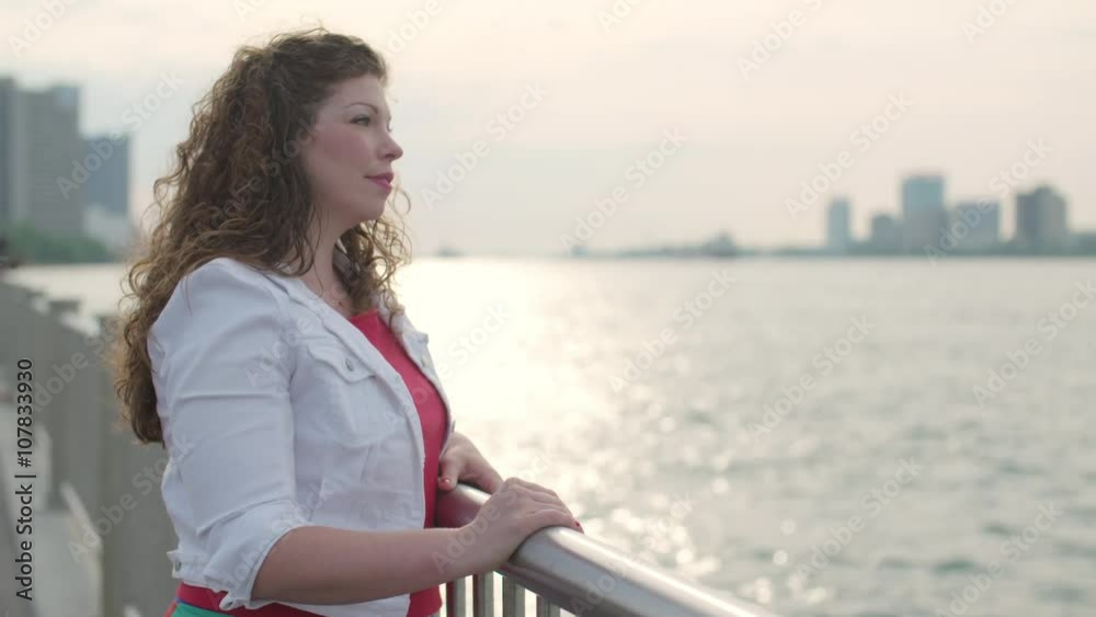 Attractive brunette waits at Detroit River side, then mixed-race boyfriend shows up and they hug. Detroit and Windsor, Ontario, skylines visible in background. Slow motion Attractive brunette waits at Detroit River side, then mixed-race boyfriend shows up and they hug. Detroit and Windsor, Ontario, skylines visible in background. Slow motion