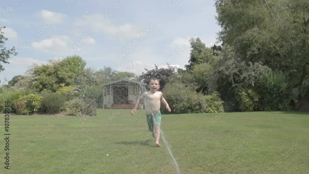 Little boy playing in a summer garden with a hose pipe and sprinkler Little boy playing in a summer garden with a hose pipe and sprinkler