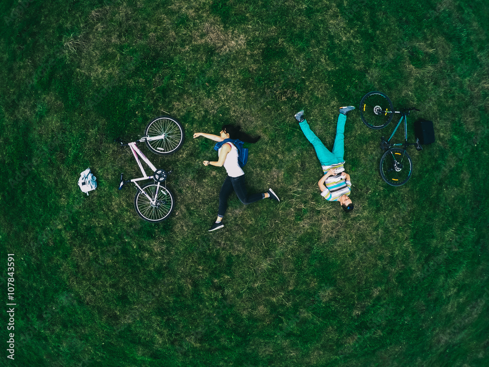 Fototapeta premium Young couple lying on the grass and biking, top view, a general