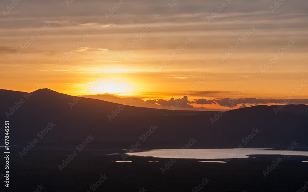 Panoramic view of huge Ngorongoro caldera (extinct volcano crater) with setting Sun against evening glow background at dusk. Great Rift Valley, Tanzania, East Africa.
