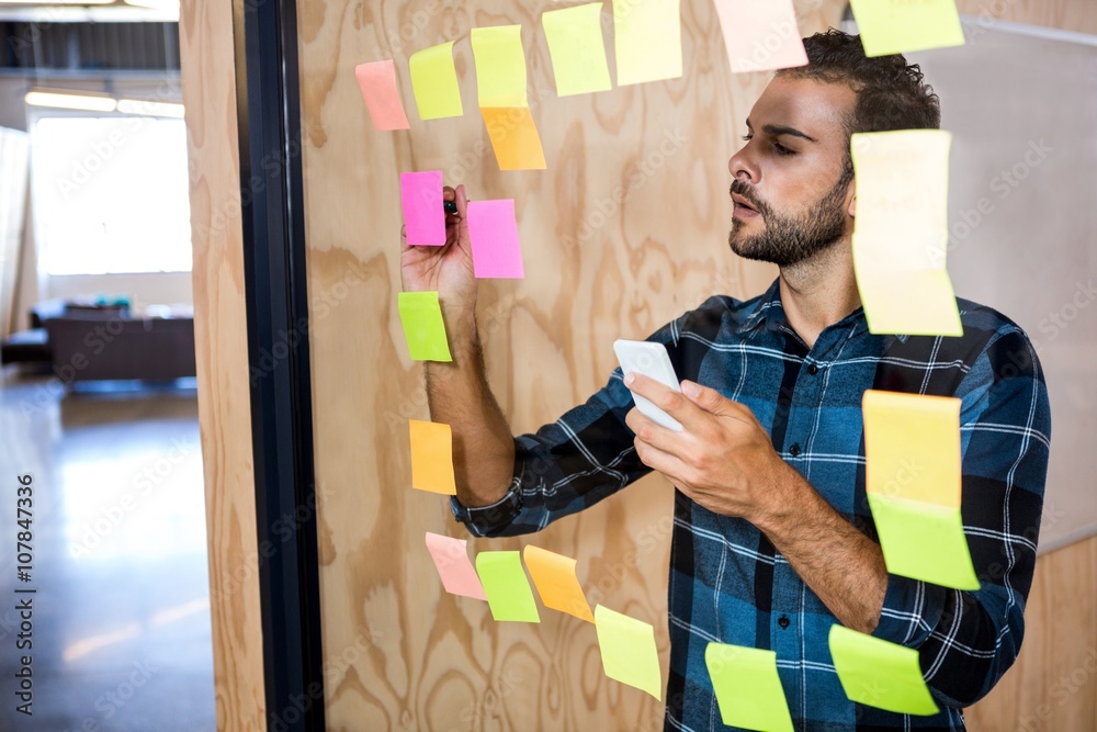 Man using mobile phone while writing on sticky notes Man using mobile phone while writing on sticky notes