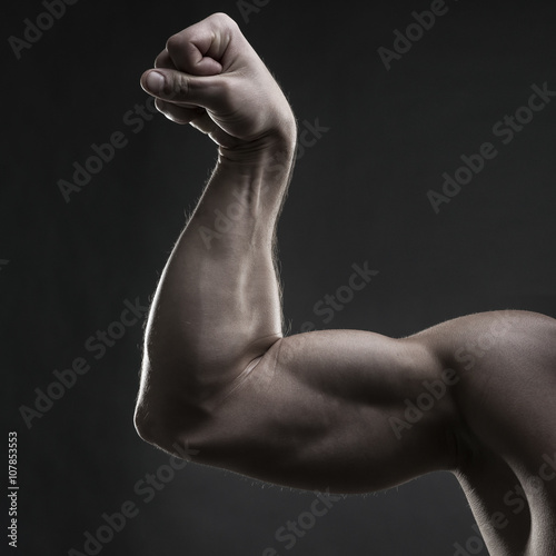Handsome muscular bodybuilder posing on gray background. Low key studio shot
