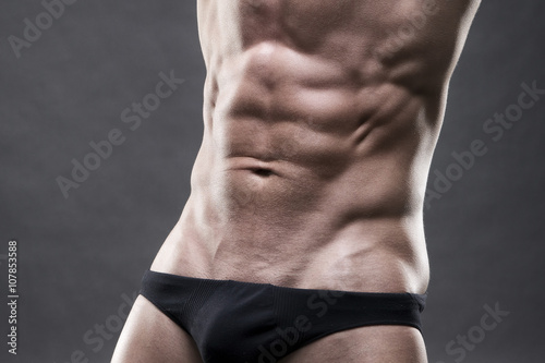 Handsome muscular bodybuilder posing on gray background. Low key close up studio shot
