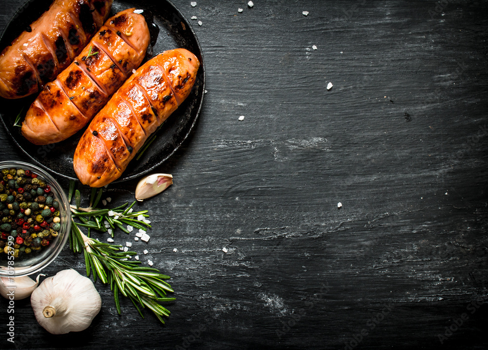 Fried sausages with garlic and herbs in a pan. - obrazy, fototapety, plakaty 