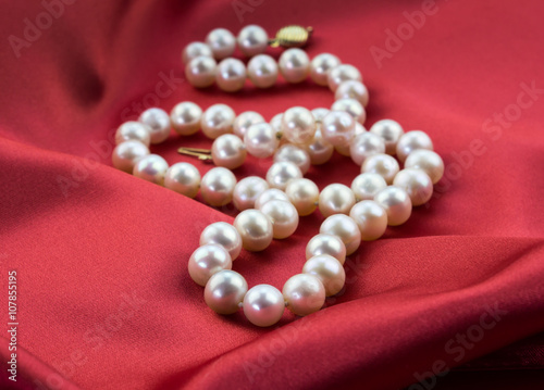 Pearl necklace isolated on red satin dress background