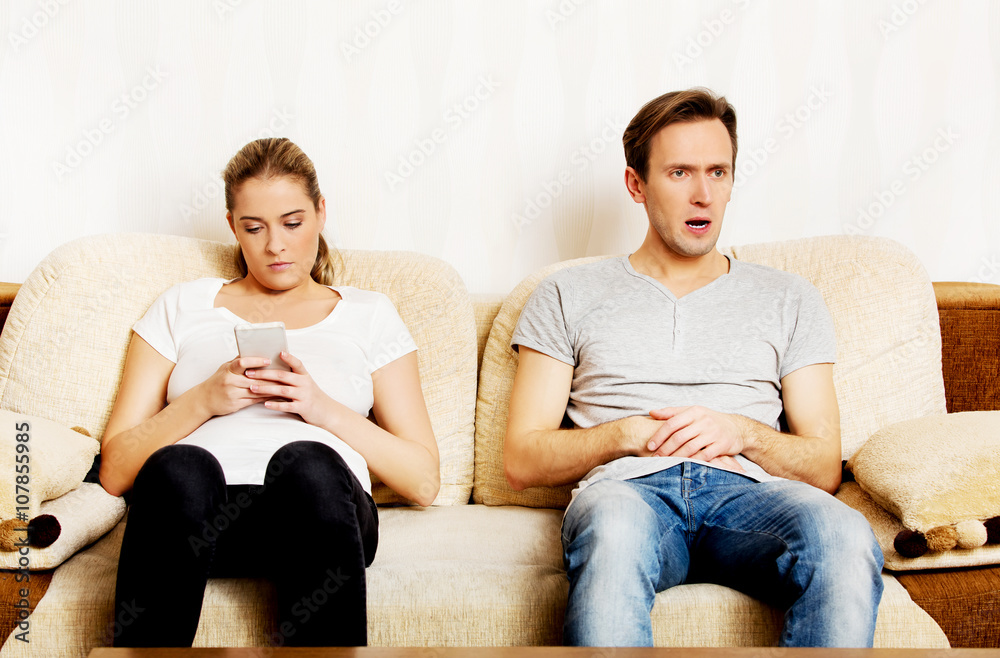 Couple at home, man watching tv woman using smartphone Couple at home, man watching tv woman using smartphone