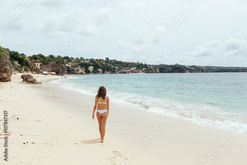 Beautiful girl in swimsuit walking along the beach.back view
