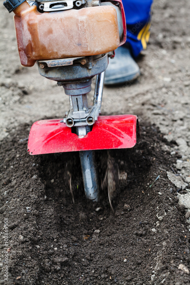 Fototapeta premium farmer plows field by tiller in spring