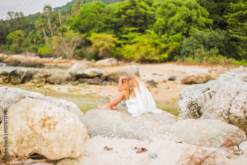 Offended sad girl with long hair sitting on a rock on the shore back 