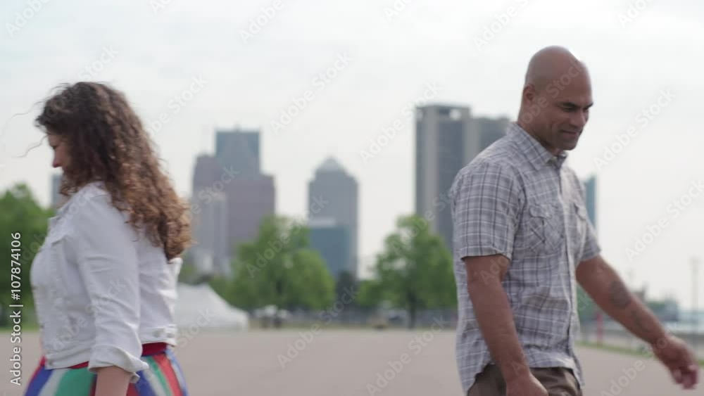 Handsome mixed-race man and attractive brunette walk past each other once, then again, against a background of the Detroit city skyline. Medium shot, slow motion Handsome mixed-race man and attractive brunette walk past each other once, then again, against a background of the Detroit city skyline. Medium shot, slow motion