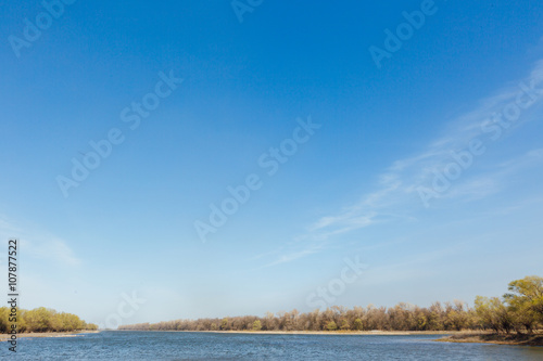 Landscape with views of the river  the trees on the shore and blue sky.