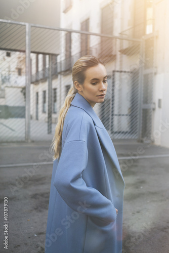 Portrait of young and attractive woman with blonde hair wearing vintage blue coat, hipster girl outdoors, film effect photo