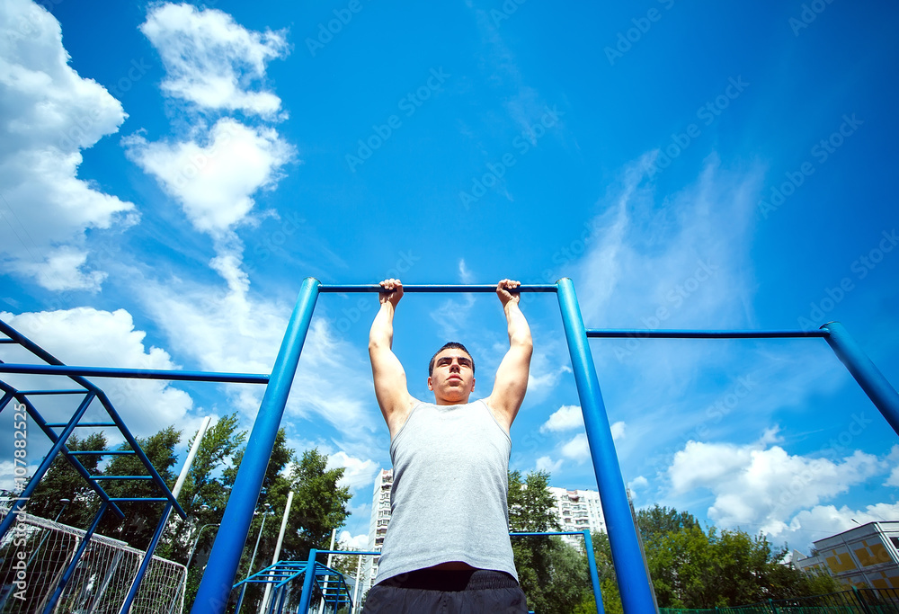 Fototapeta premium Muscular man doing pull-ups on horizontal bar