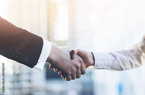 Closeup image of business partners making handshake outdoors, modern office or skyscrapers on the background, flare light