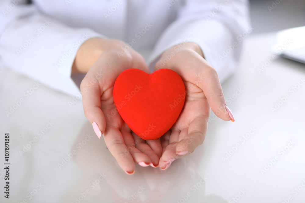 Female doctor with stethoscope holding heart. Patients couple sitting in the background Female doctor with stethoscope holding heart. Patients couple sitting in the background