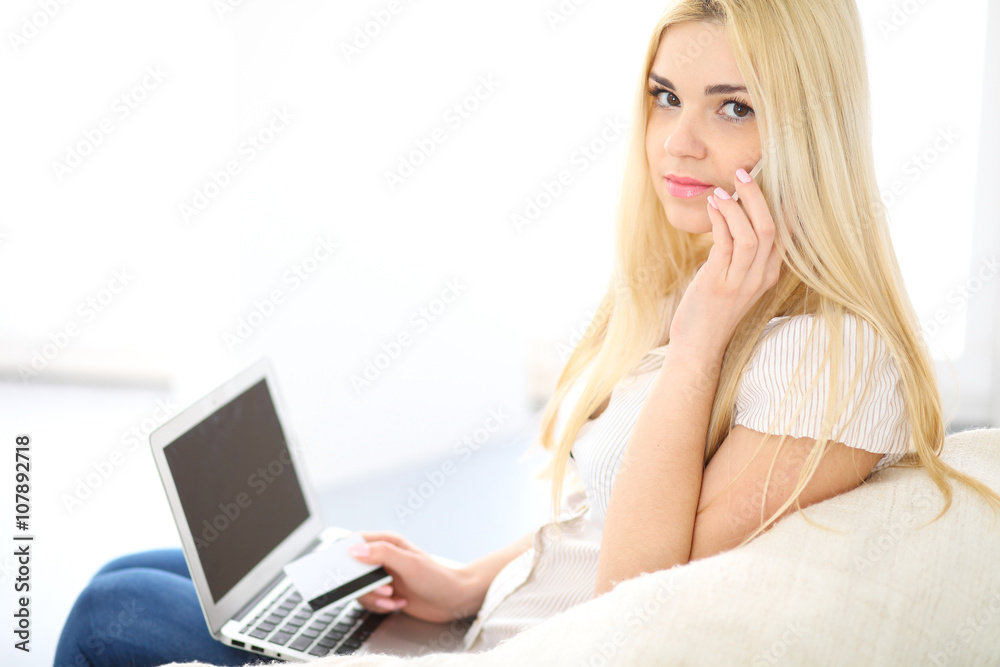 Happy woman doing online shopping at home . Close- up of a hand holding a credit card next to a laptop Happy woman doing online shopping at home . Close- up of a hand holding a credit card next to a laptop