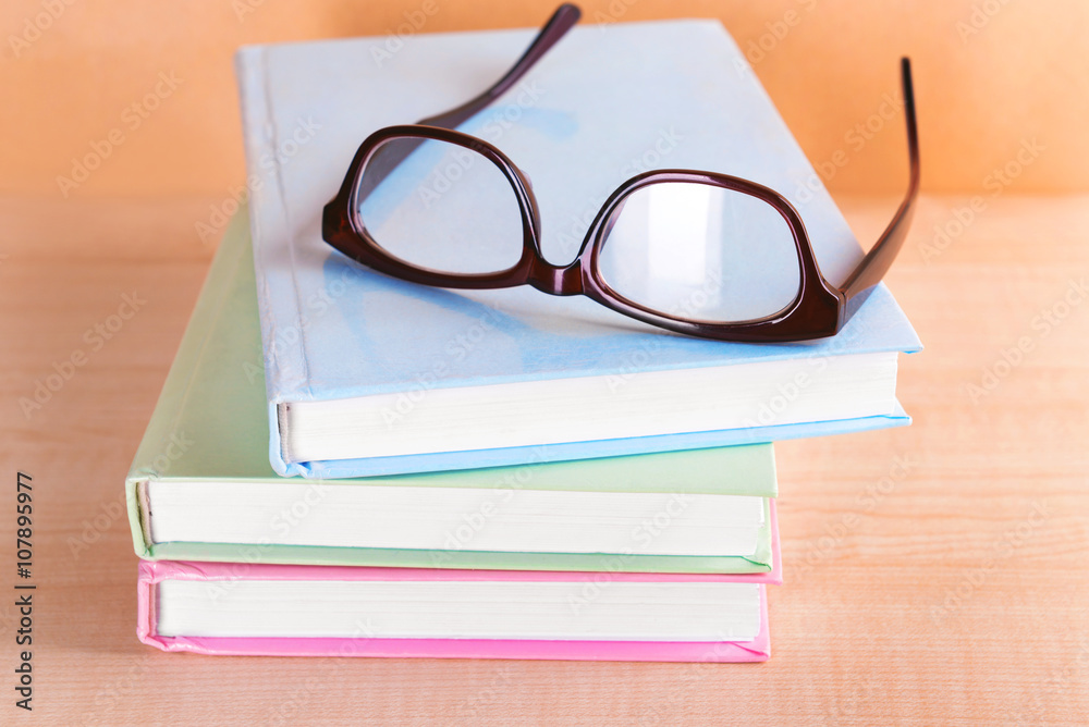 Pile of books and eyeglasses on it against beige background Pile of books and eyeglasses on it against beige background