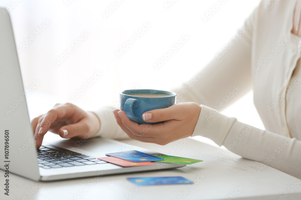 Fototapeta premium E-commerce concept. Woman with credit card, laptop and cup of coffee, close up