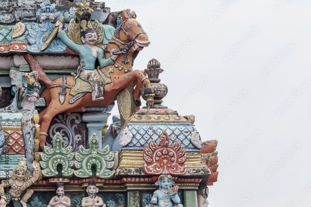 Trichy, India - October 15, 2013: Closeup of  decoration on one Gopuram at Shirangam temple. Fighting man on brown horse seems to jump off the temple. Pastel colors, gray sky.