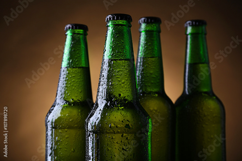 Four green glass bottles of beer on dark lighted background, close up