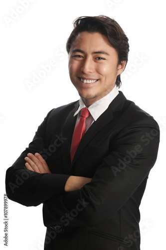 Smiling businessman looking at camera, wearing a black suit, white shirt and a red tie. Standing in front of a white background.