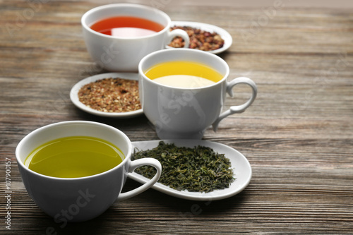 Tea concept. Different kinds of dry tea in ceramic bowls and cups of aromatic tea on wooden background