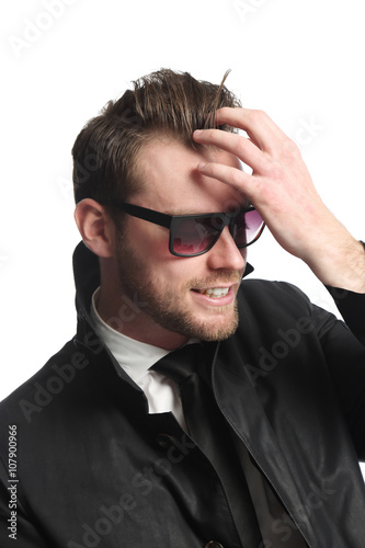 Portrait of an attractive and trendy man sitting down with a white background, wearing a black jacket, white shirt, black tie and dark sunglasses. Looking away from camera.