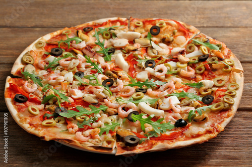 Pizza with seafood, red pepper and olives on wooden table