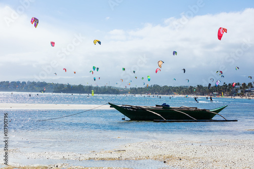 Kitesurfers enjoying wind power on Bulabog beach, Boracay island, Philippines. Empty boat moored in foreground.