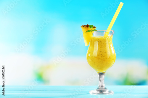 Pineapple smoothie in cocktail glass with slices on blue blurred background