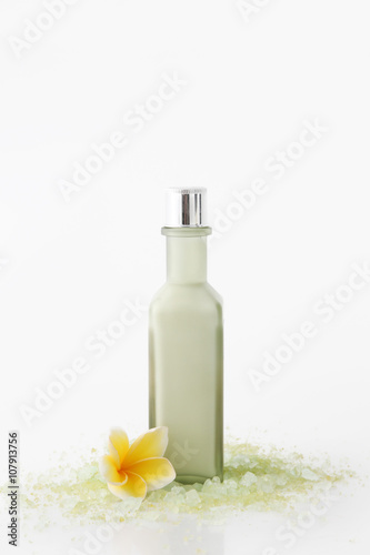 Green cosmetic bottle with bath salt and frangipani flowers