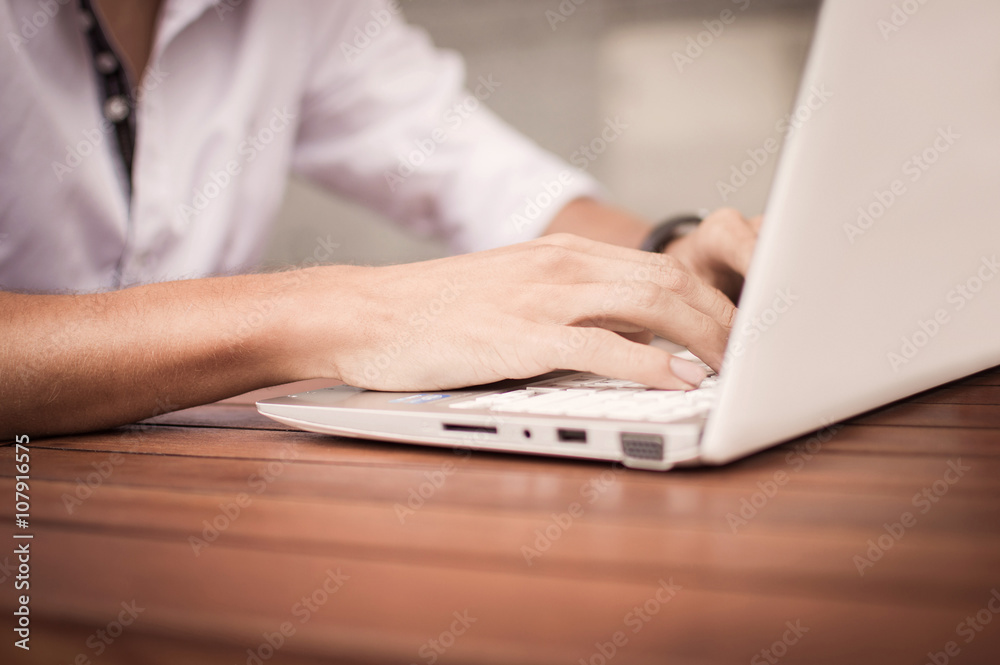 Cropped image of a young man working on his laptop in a coffee shop, using laptop at office desk, young male student typing on computer sitting at wooden table