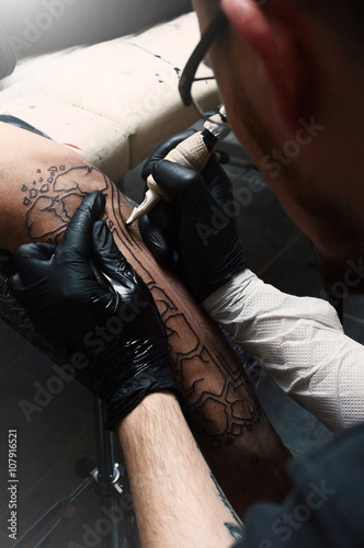 Tattoo artist does the tattoo on his hand man. Closeup.