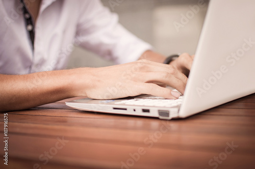 Cropped image of a young man working on his laptop in a coffee shop, using laptop at office desk, young male student typing on computer sitting at wooden table